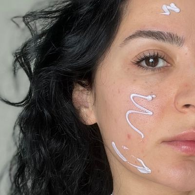 Close-up of one side of iclal's face showing a swatch of purple color corrector on her cheek before blending